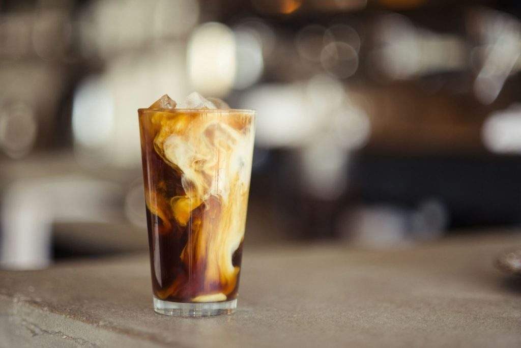 Segelas es kopi susu dingin dengan lapisan kopi dan susu di cafe