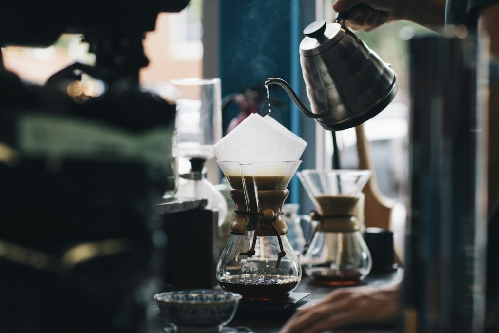 Air panas dituangkan ke bubuk kopi dalam alat pour over di meja kayu
